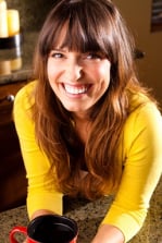 A woman holds a cup of coffee and smiles